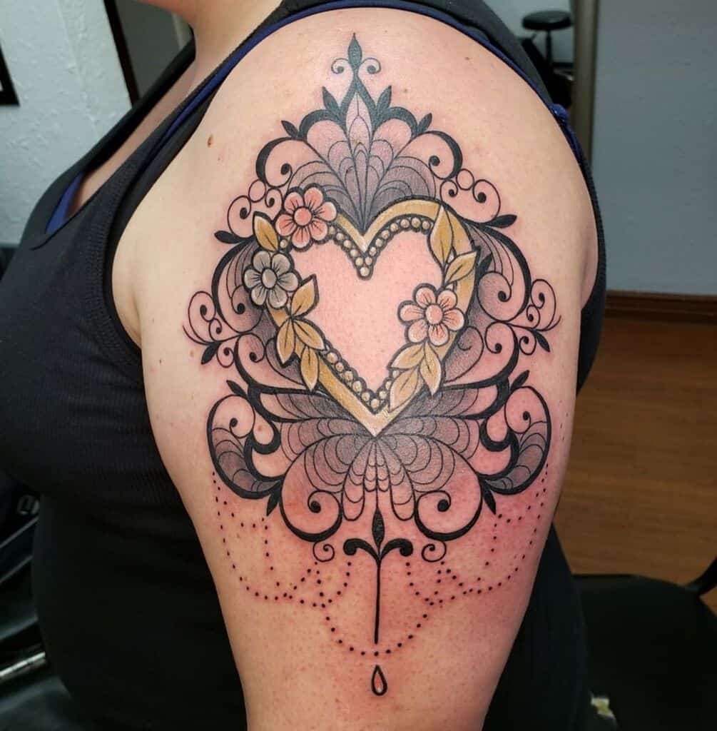 Elegant upper arm tattoo featuring an ornate heart-shaped frame adorned with flowers, pearls, intricate filigree, and chandelier-style beadwork