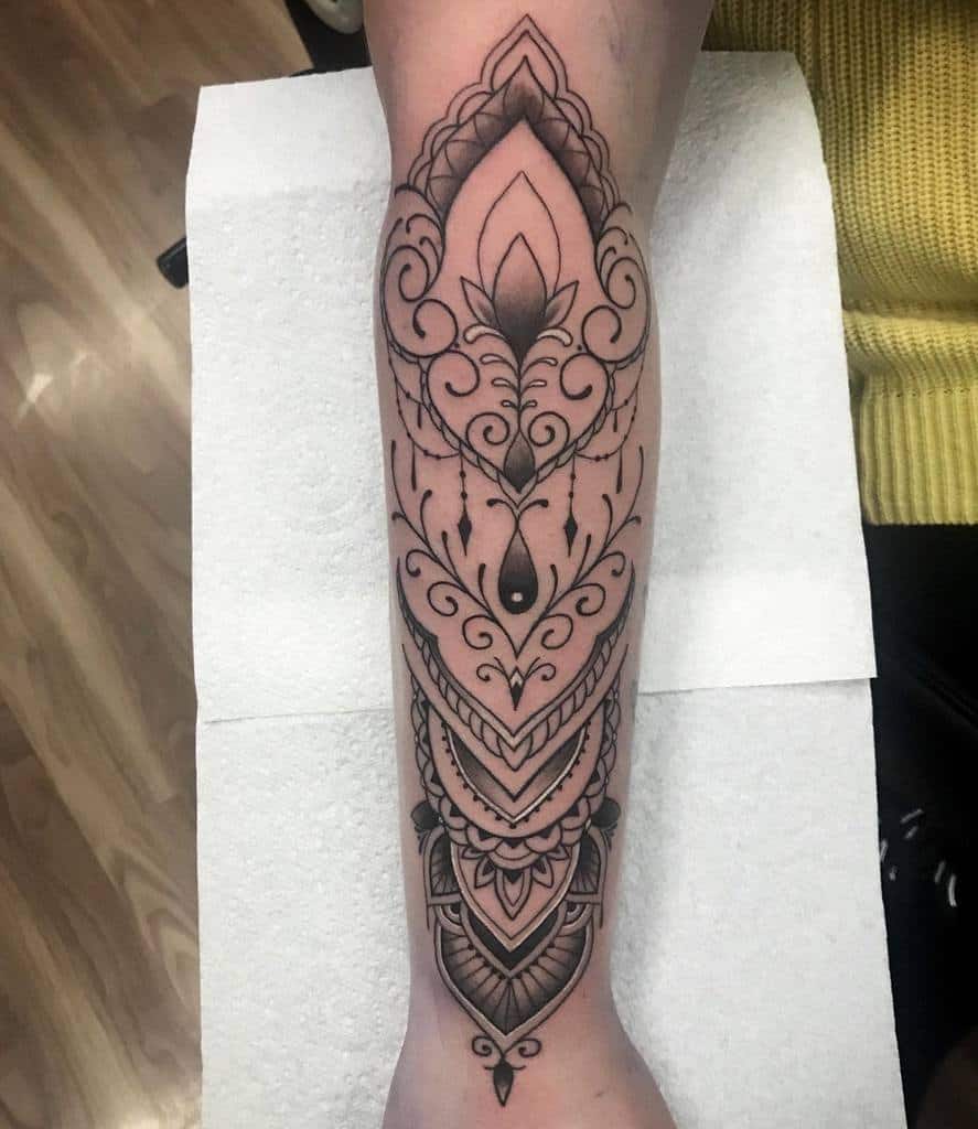 Intricate black ink forearm tattoo featuring symmetrical ornamental patterns, mandala elements, chandelier-style beadwork, and teardrop accent