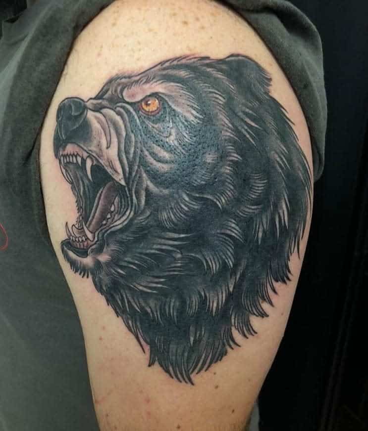 Tattoo of a majestic bear's head roaring fiercely on a person's upper arm