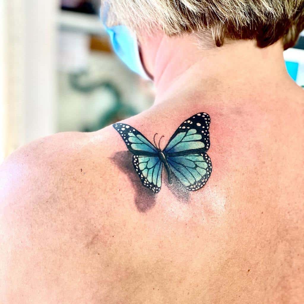 A person adorned with a delicate blue butterfly tattoo on the upper back