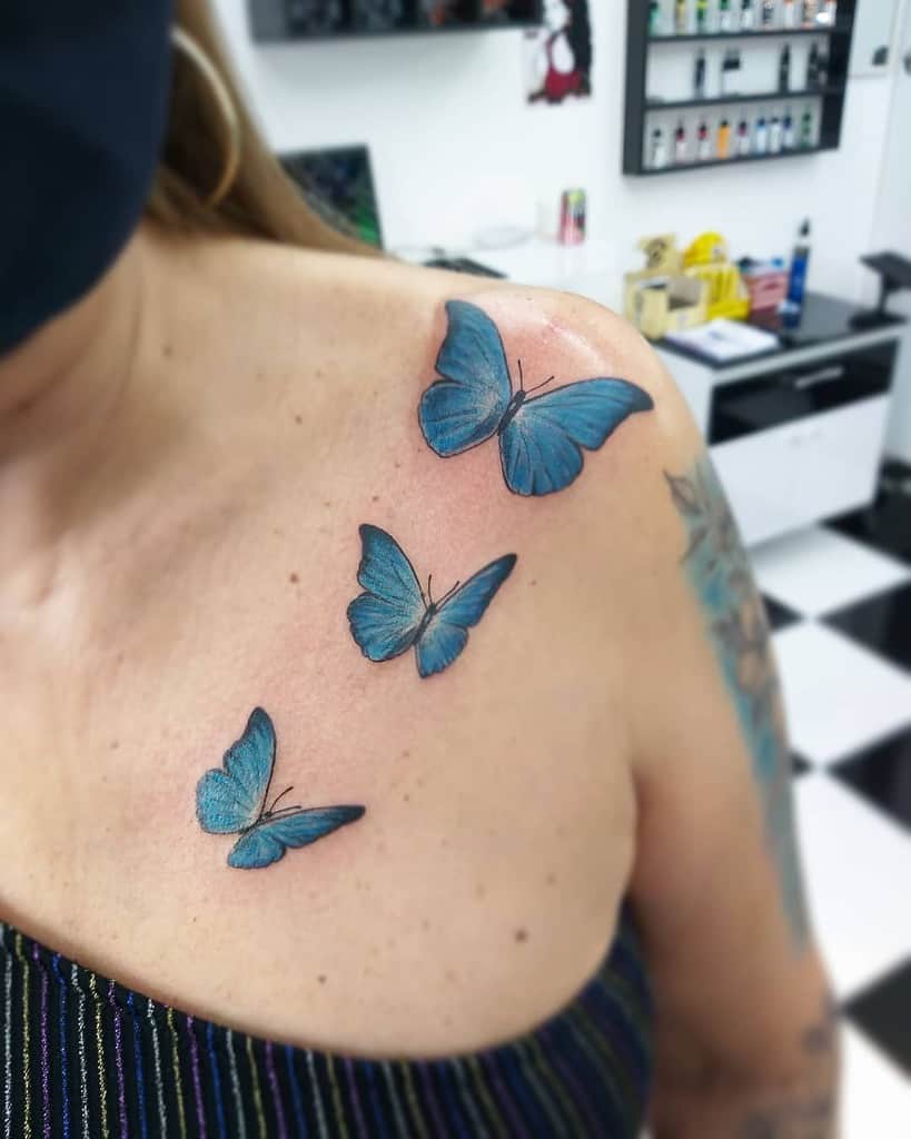 Tattoo of three stunning blue butterflies gracefully spread across a woman's upper chest