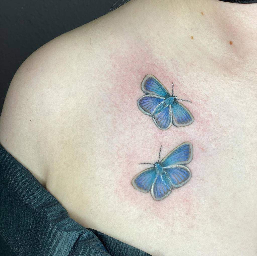 Two blue butterfly tattoos delicately inked on a woman's upper chest near the shoulder