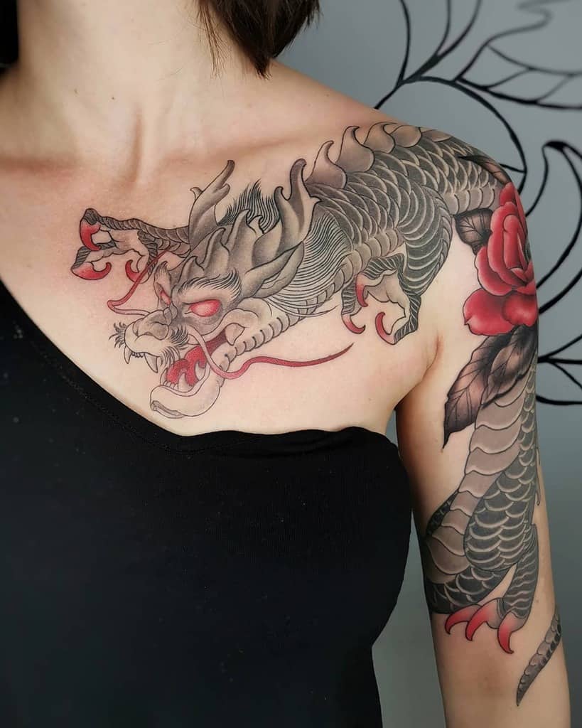 Tattoo of a dragon with red eyes and a red rose on a woman's shoulder and arm