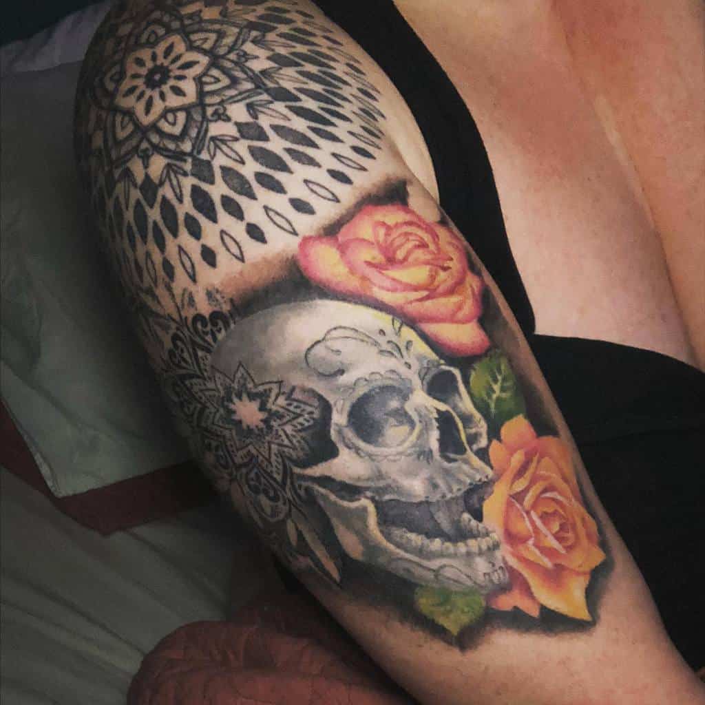 Arm tattoo featuring a skull, orange roses, and intricate mandala designs