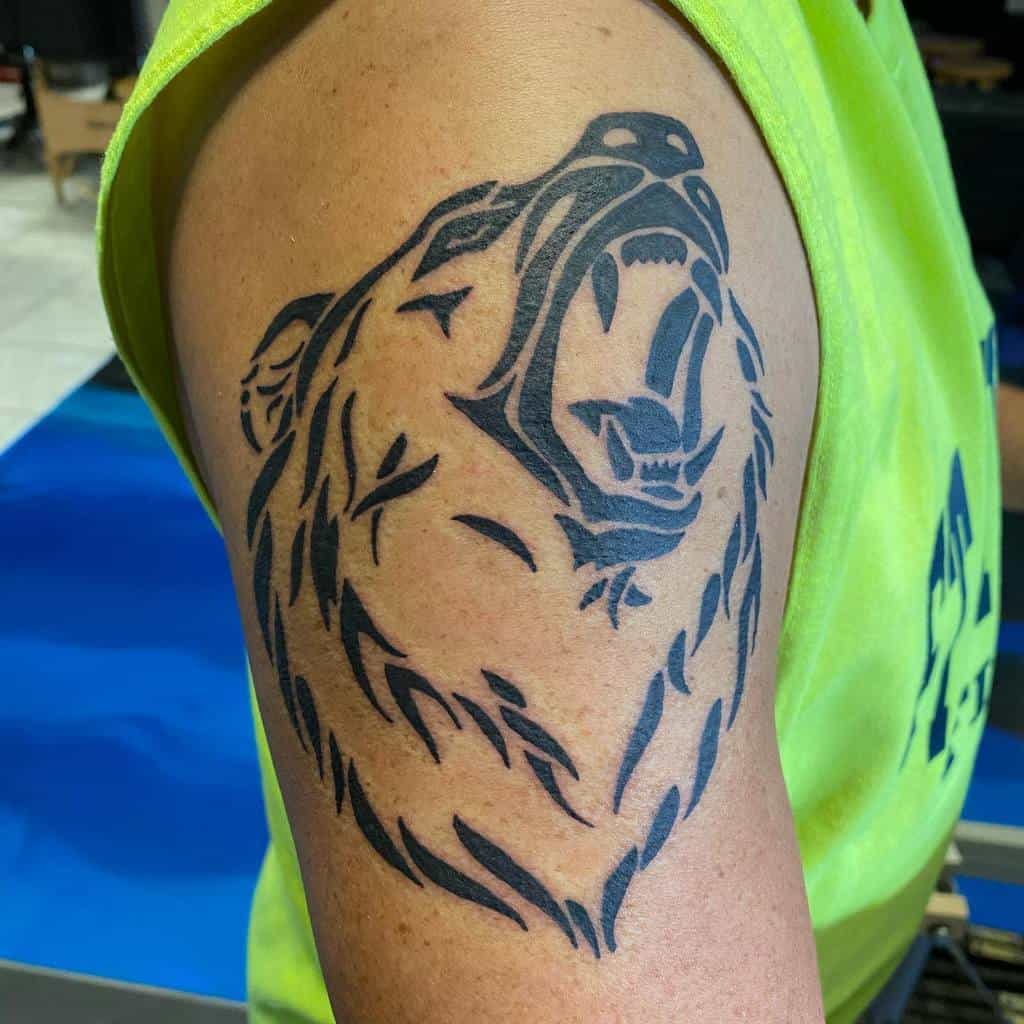 A tattoo of a roaring bear's head sprawls across the upper arm