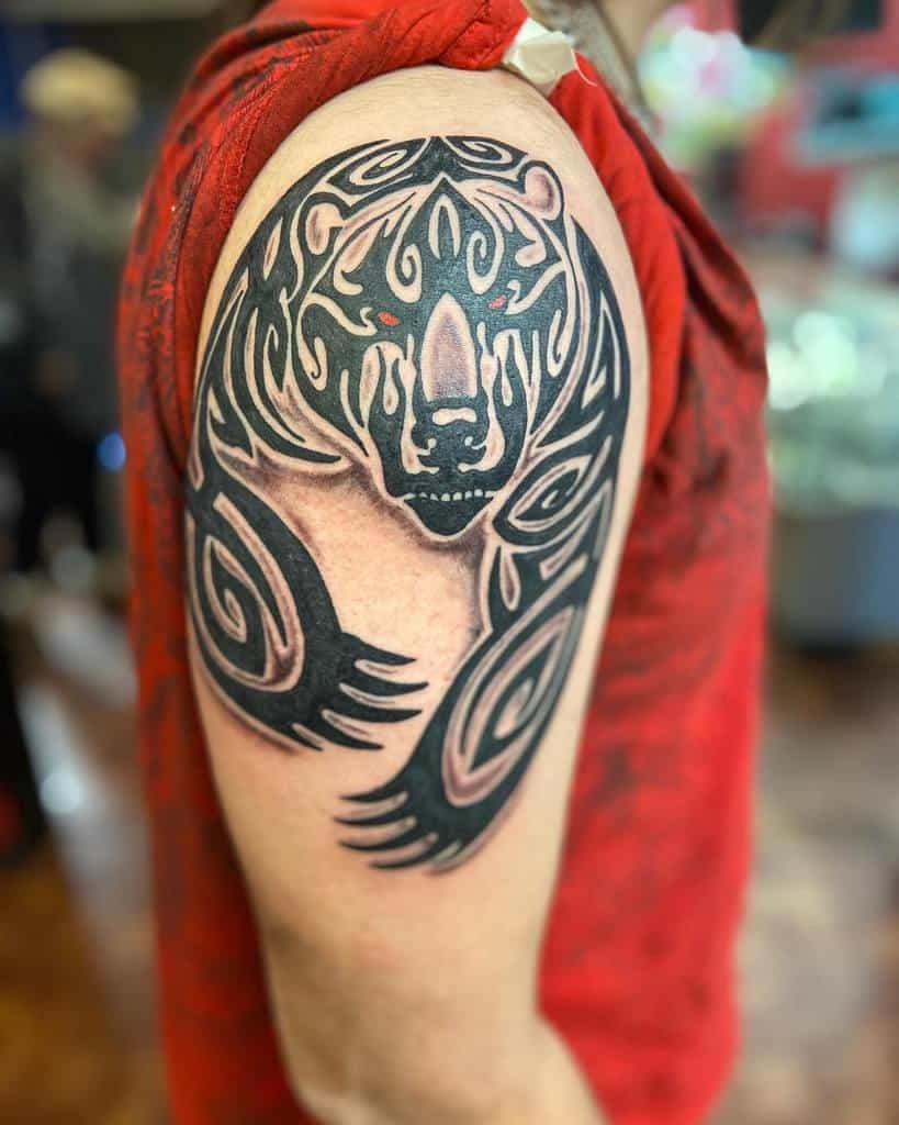 A tribal-style bear with red eyes tattoo graces the upper arm