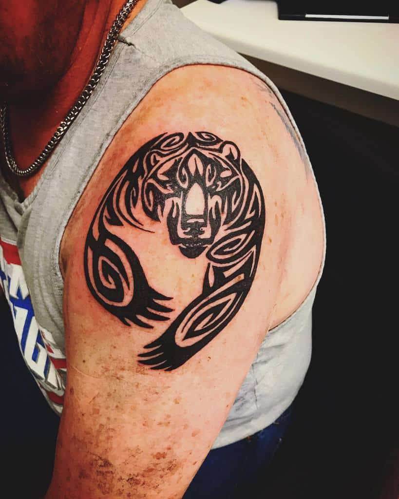 A tribal bear tattoo in bold black ink adorns the person's upper arm, perfectly complementing their edgy chain necklace