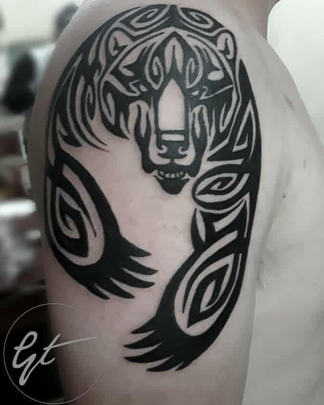 A tribal tattoo on the upper arm showcases a majestic bear, crafted with bold black lines and intricate patterns