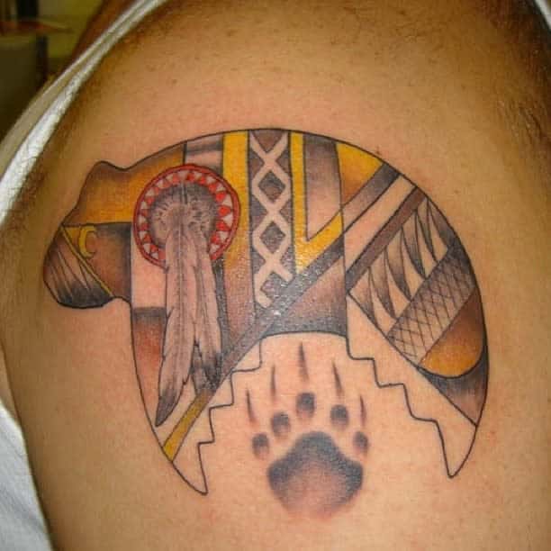 Tattoo of a tribal bear with feathers and a paw print on an upper arm