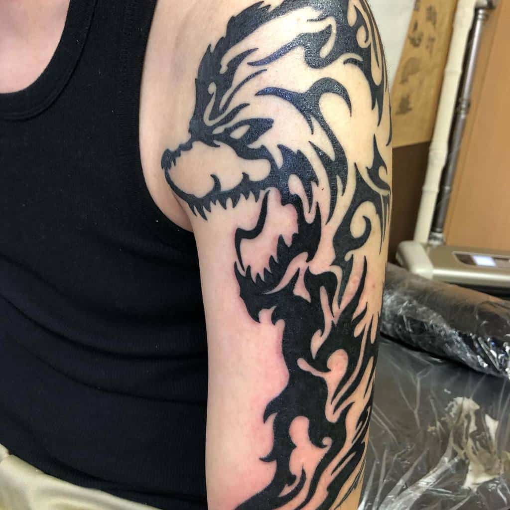 A tribal-style tattoo of a wolf, accentuated with flames and a hint of bear elements, adorns a person's upper arm