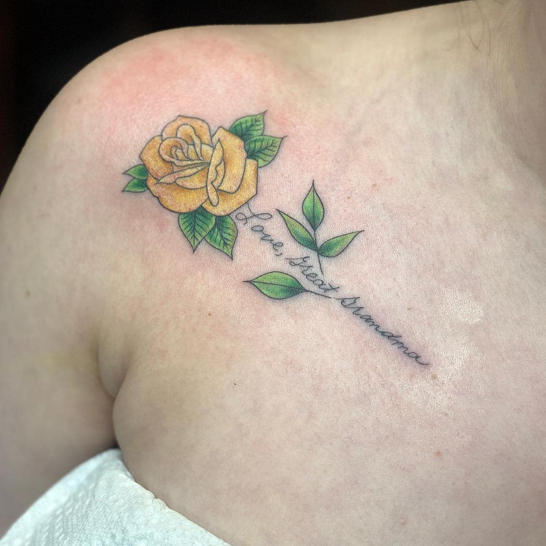 A yellow rose tattoo with green leaves and the script "Love great Grandma" on an upper chest