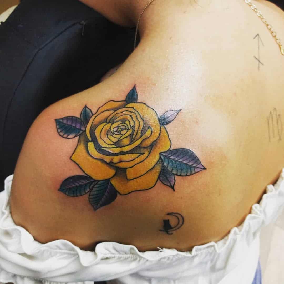 A yellow rose tattoo with green leaves on a shoulder