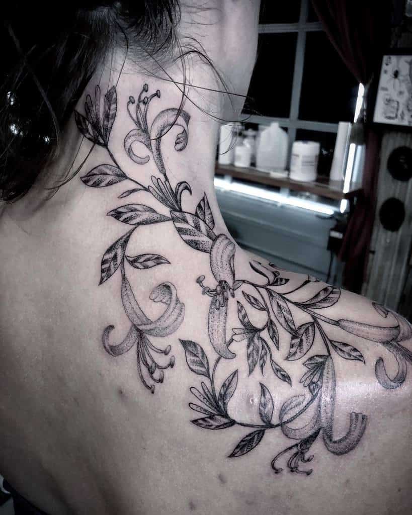 Elegant tattoo on the upper back and neck features delicate honeysuckle flowers and leaves in a black and grey style