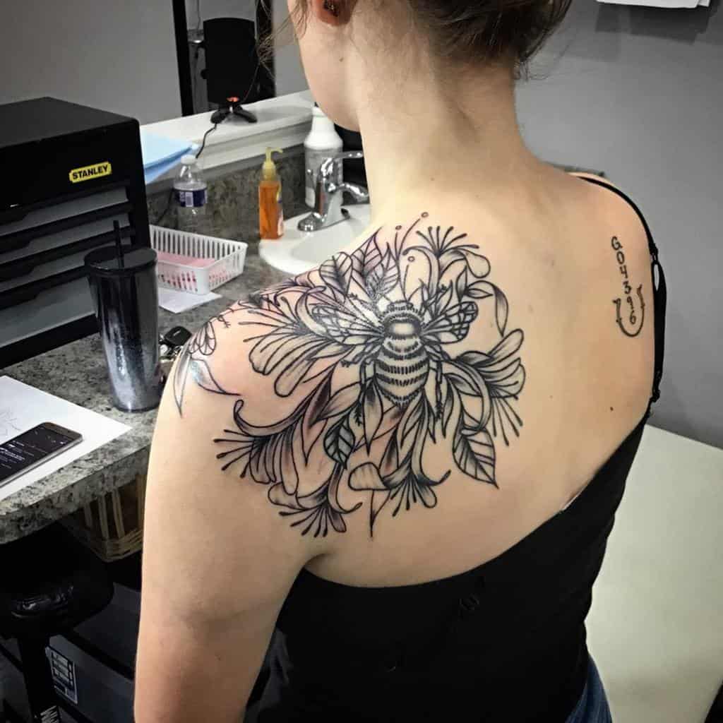 Large bee and honeysuckle floral tattoo on woman's upper back and right shoulder blade