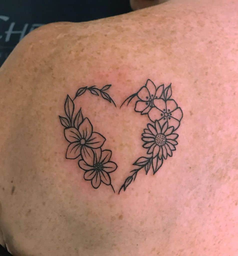 Shoulder tattoo black and grey fine line traditional daisies and other flowers forming heart-shaped wreath