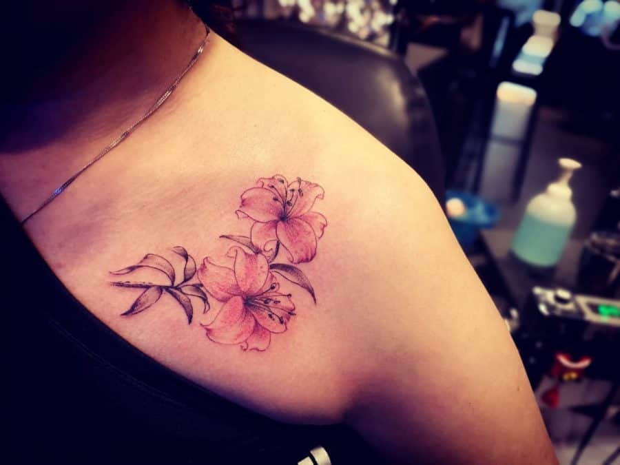 Pink floral tattoo of lilies on the shoulder in a tattoo studio