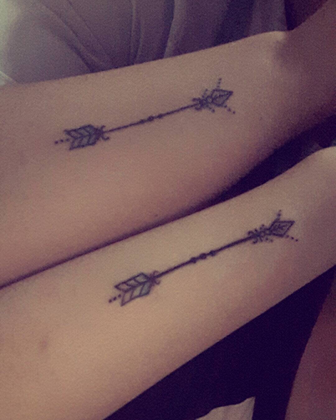 Two arms with matching arrow tattoos pointing towards each other