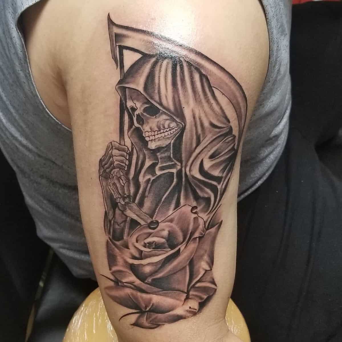 Santa Muerte tattoo with a scythe and rose, detailed black-and-grey shading for a bold, eerie look