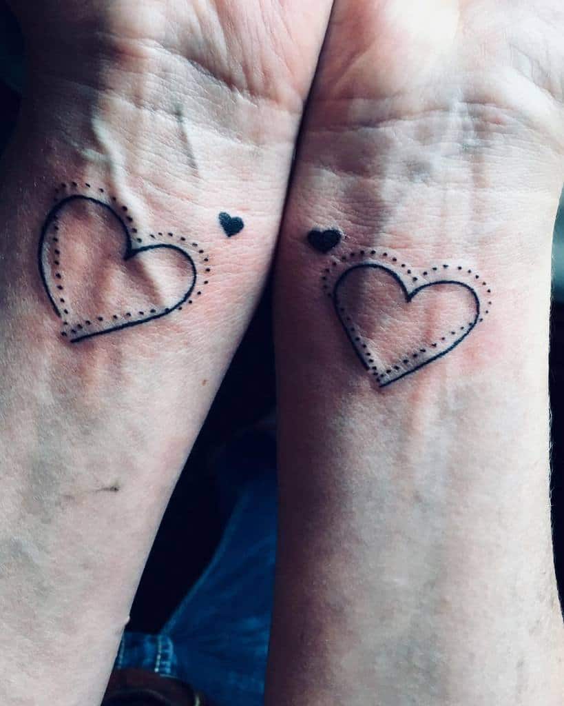 Two wrists with matching tattoos: dotted outline hearts and small solid black hearts above them