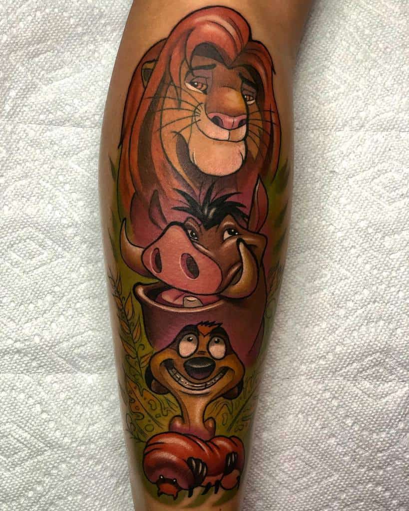 Colorful tattoo featuring Simba, Timon, and Pumbaa in a stacked pose, with vibrant shading and surrounded by lush green leaves