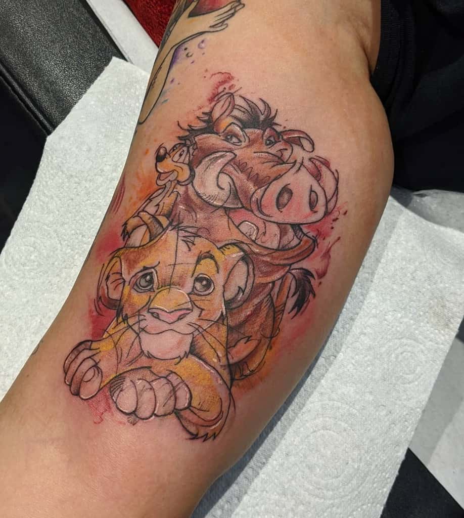 Colorful tattoo of Simba, Timon, and Pumbaa in a playful pose, surrounded by red and orange watercolor splashes