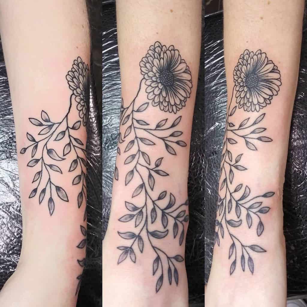 Black ink floral tattoo of an aster with leaves on forearm