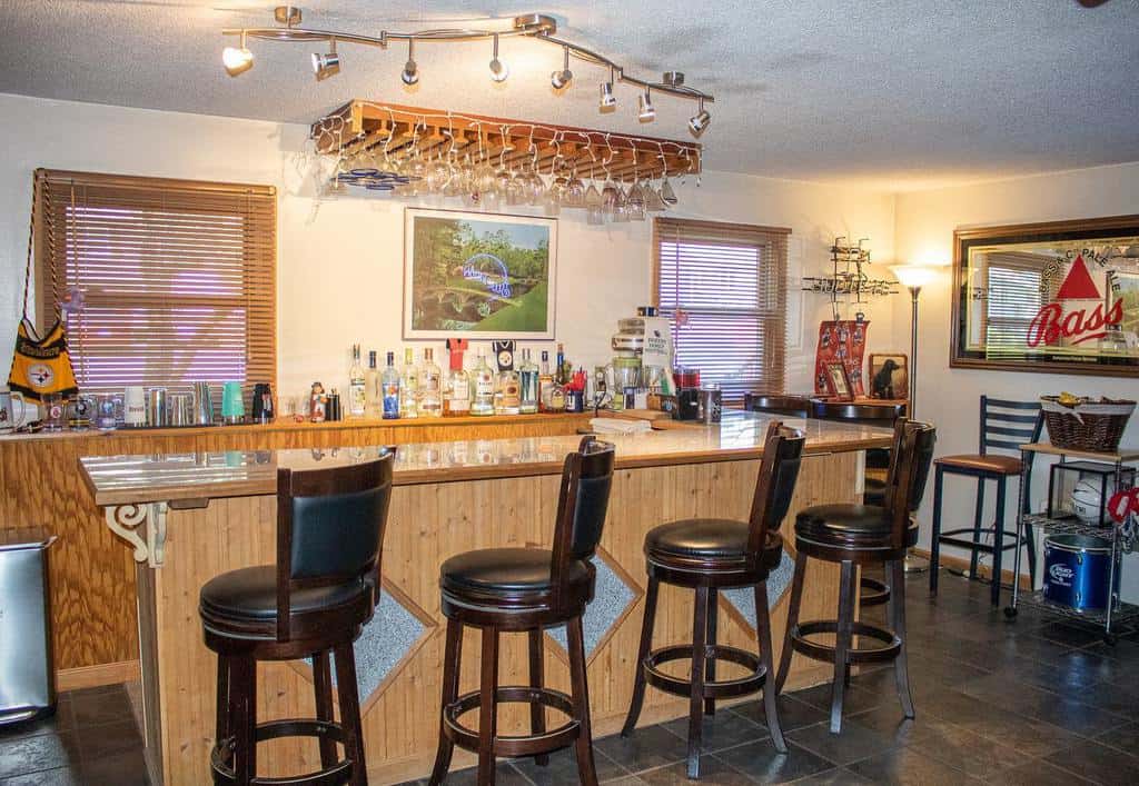 Simple basement bar with wooden bar counter, leather stools, and overhead glass rack.