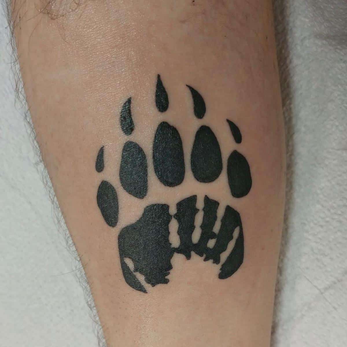 A black bear paw tattoo with a silhouetted forest scene adorns a person's forearm, intricately blending nature and artistry