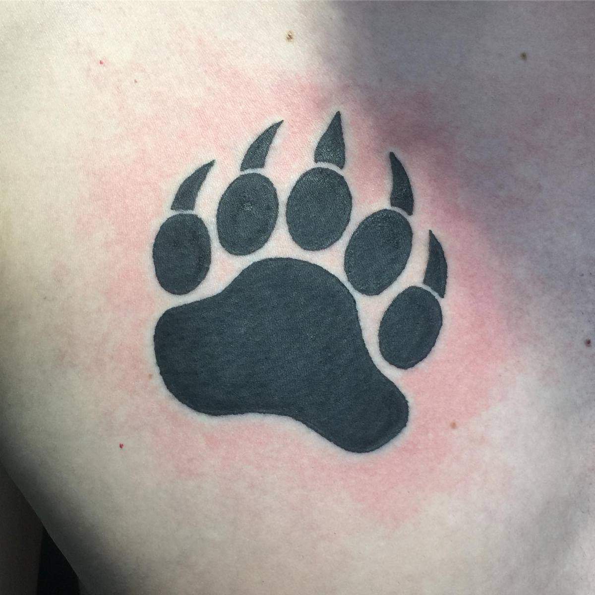 A black bear paw tattoo with a slightly red area surrounding it