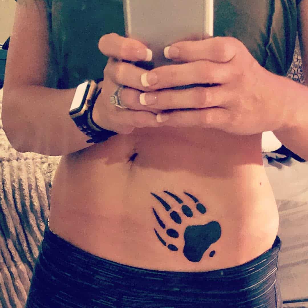 A person taking a selfie, displaying a bear paw tattoo on their lower abdomen