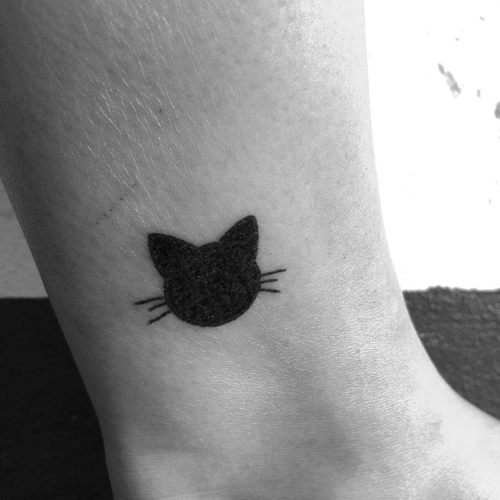 Minimalist black cat face tattoo on an ankle