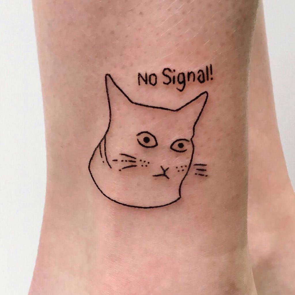 Ankle tattoo of a minimalist cat face with the phrase 'No Signal!' above it, drawn in a simple black line style