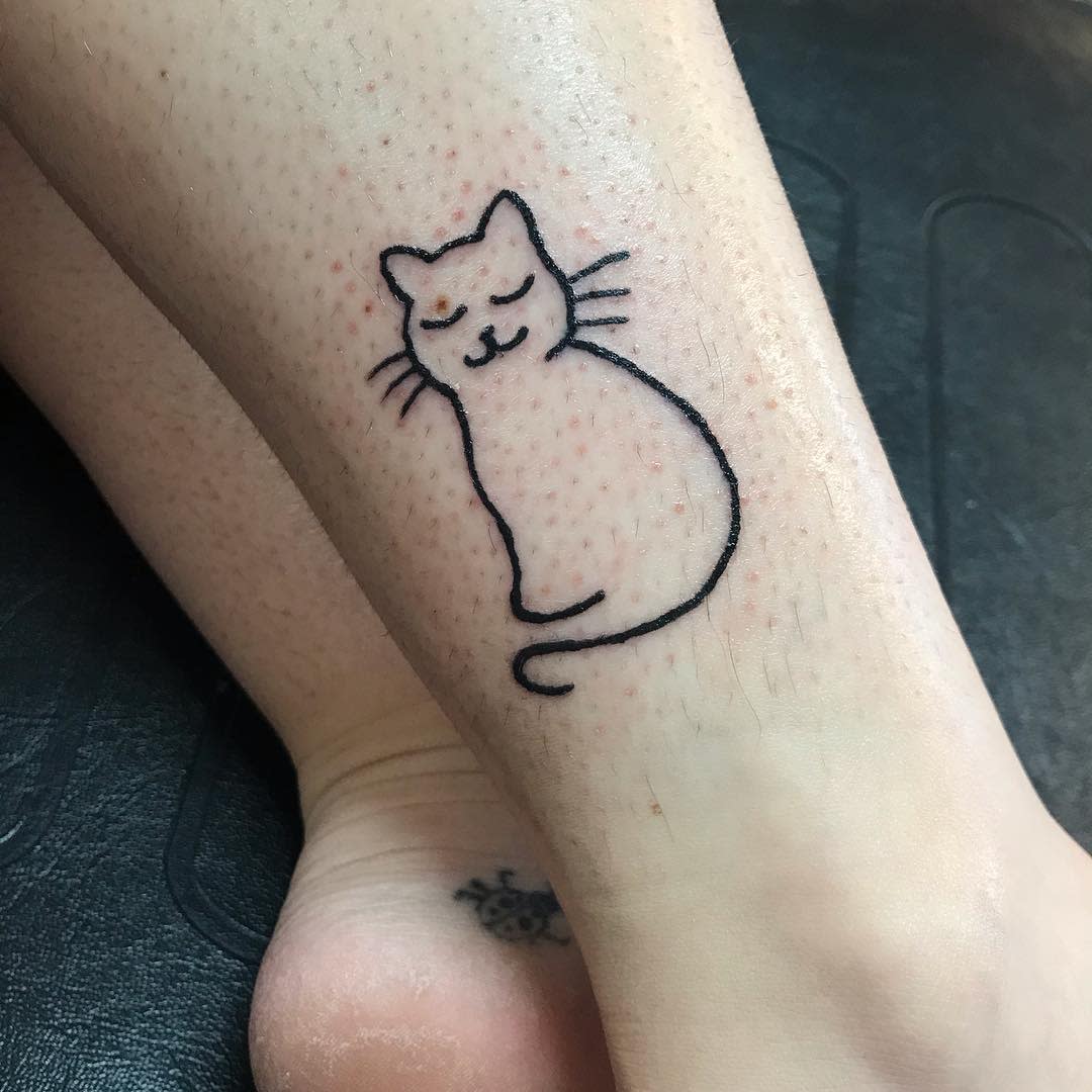 Simple black outline tattoo of a content cat on an ankle