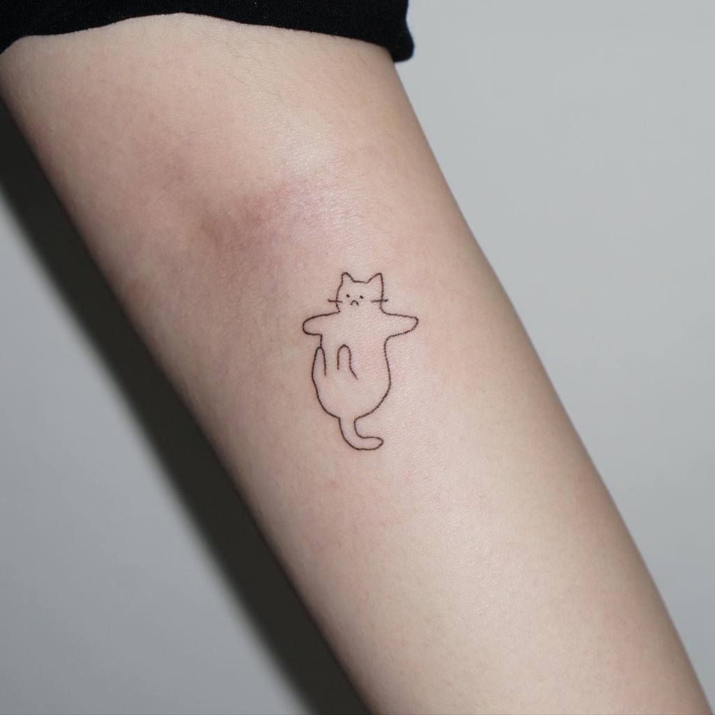 Simple line tattoo of a cat lying on its back on a person's arm