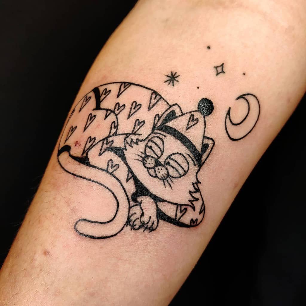 Tattoo of a sleeping cat in pajamas with hearts, moon, and stars on an arm