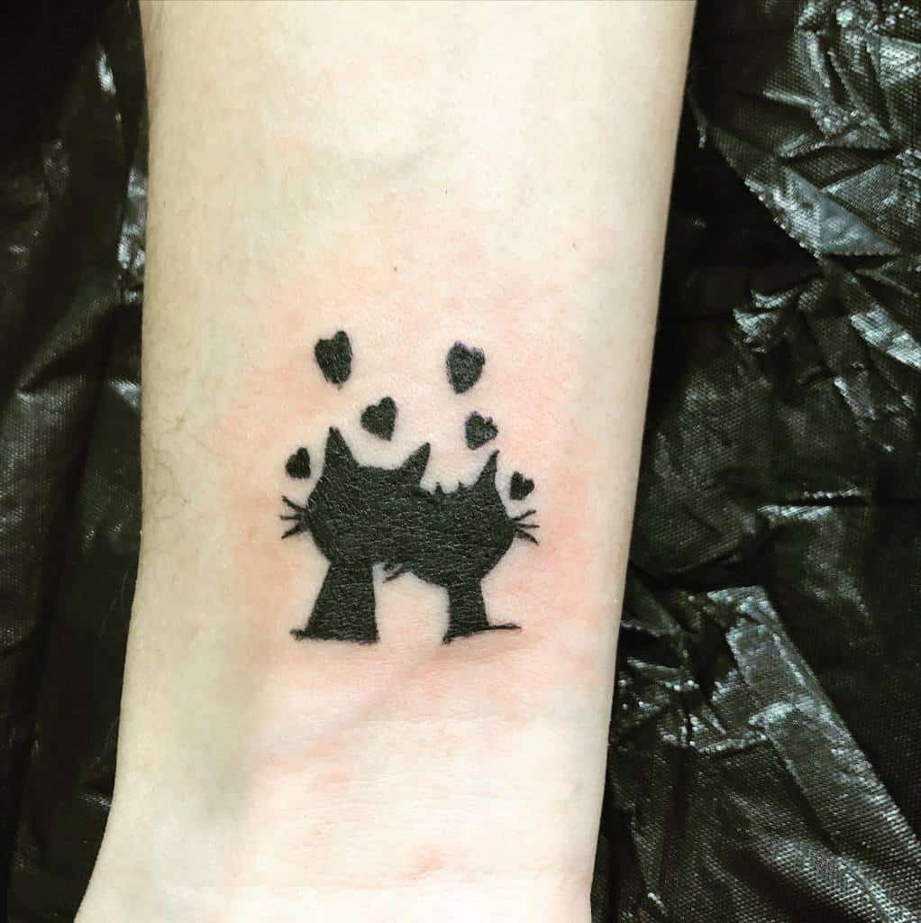 Tattoo of two cats with heart shapes above them on an arm