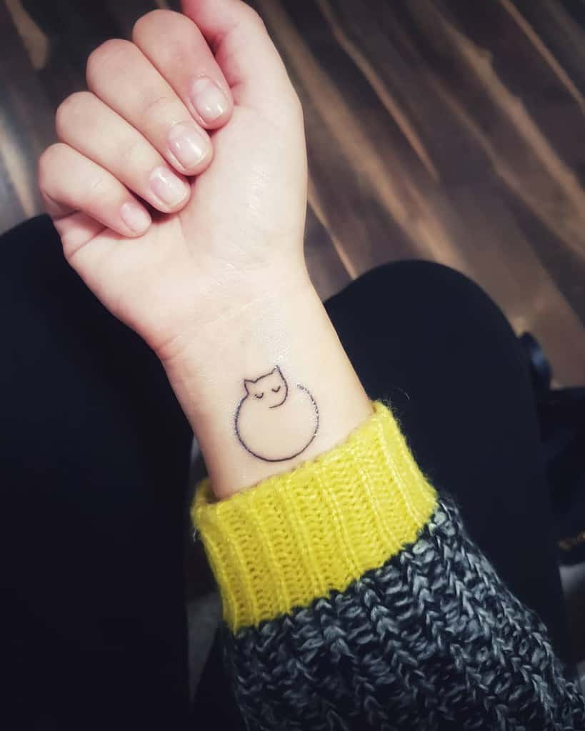 A wrist with a simple cat face tattoo