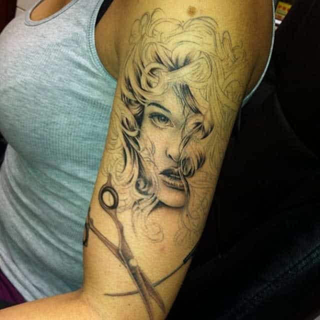 Half sleeve tattoo of a woman's face and scissors on a person's upper arm