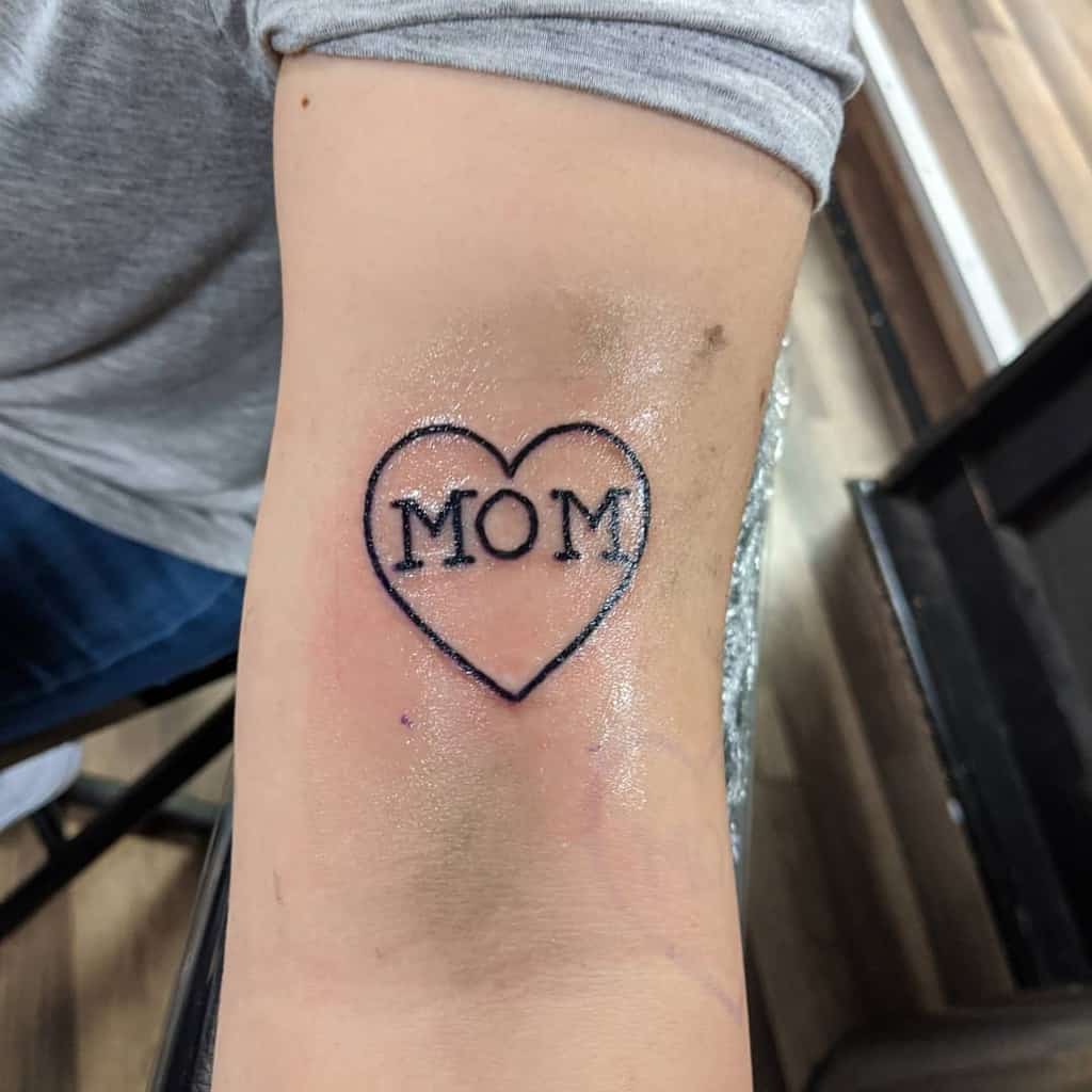 Tattoo of a radiant heart with "MOM" elegantly inscribed inside it, placed on a person's inner arm