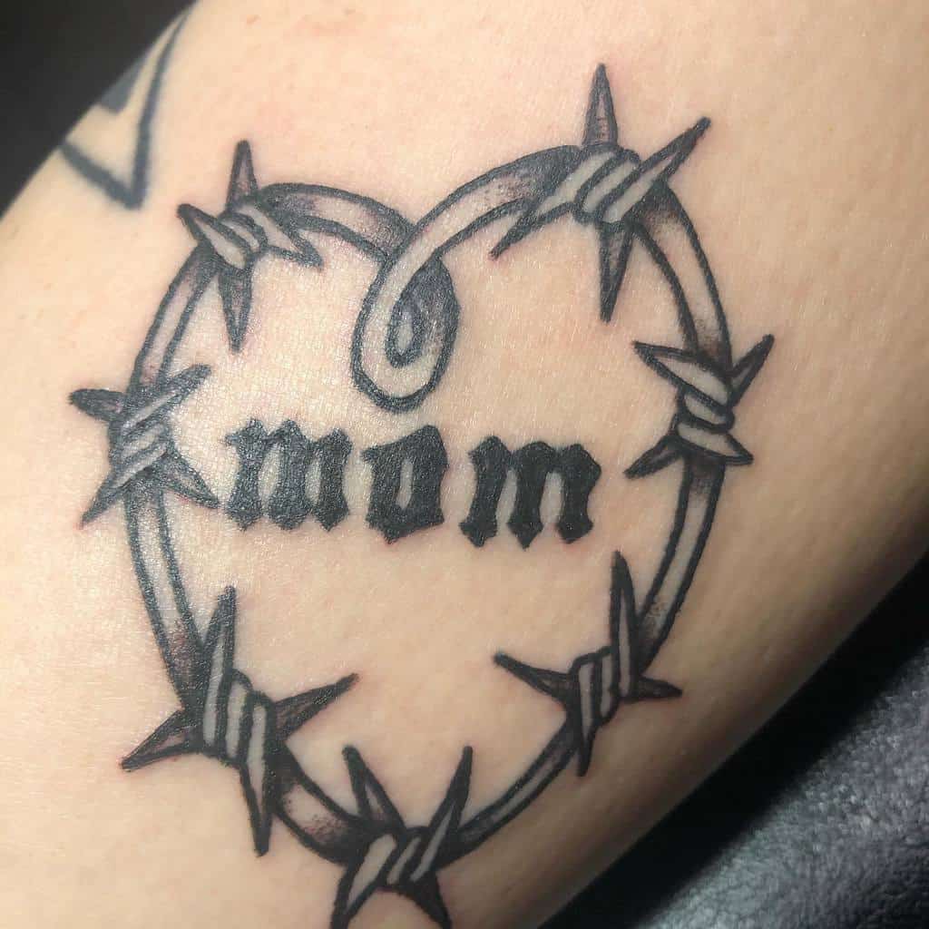 Tattoo of a barbed wire heart with "mom" elegantly inscribed in the center
