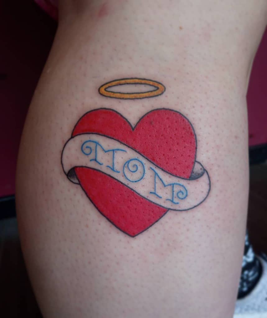 Tattoo featuring a vibrant red heart adorned with a "MOM" banner, crowned by a radiant gold halo