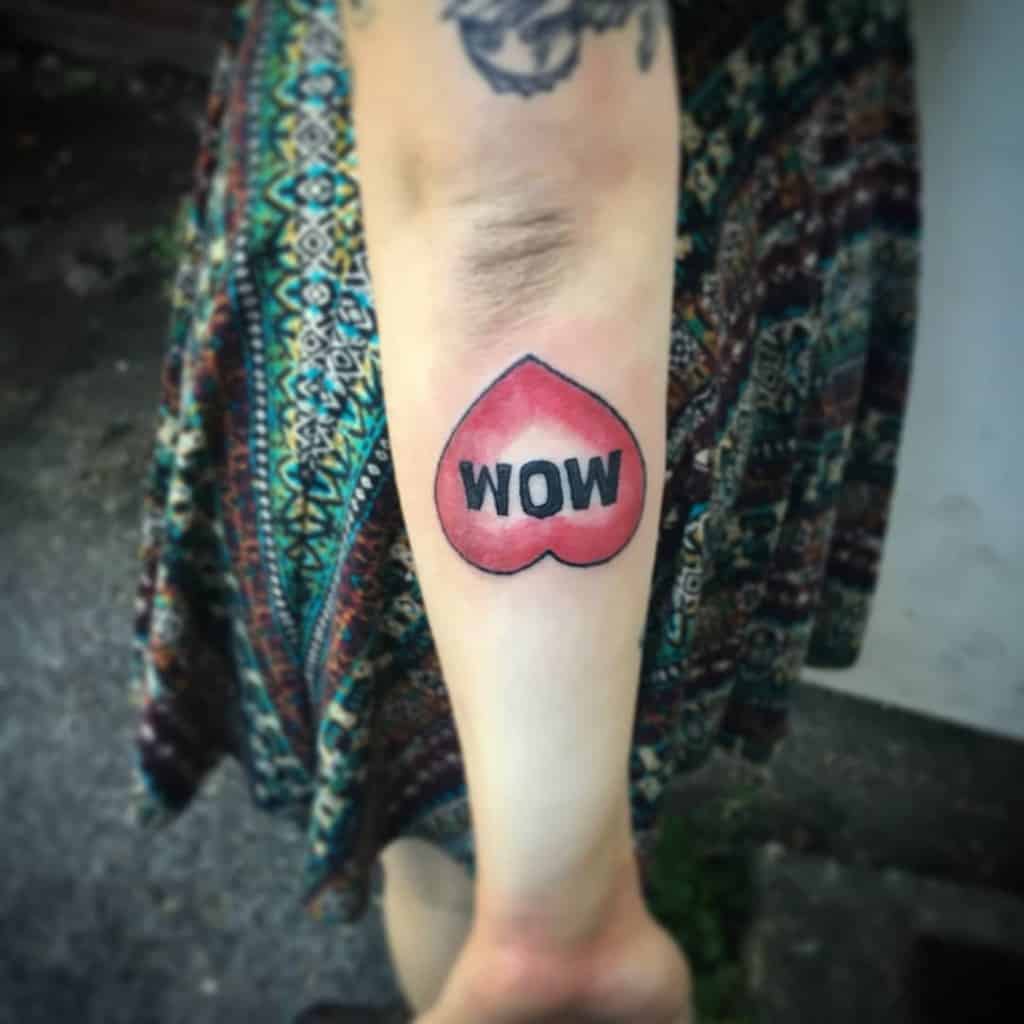 Arm tattoo of a red heart with the word "WOW" in the center, person wearing a patterned dress, symbolizing their love for their mom