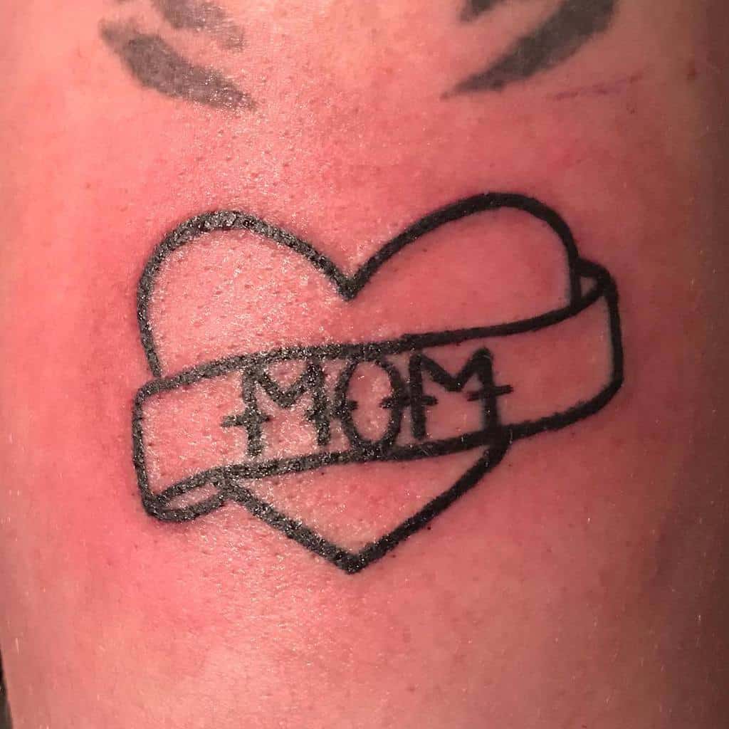 A heart tattoo featuring the word "MOM" elegantly written inside a banner draped across it