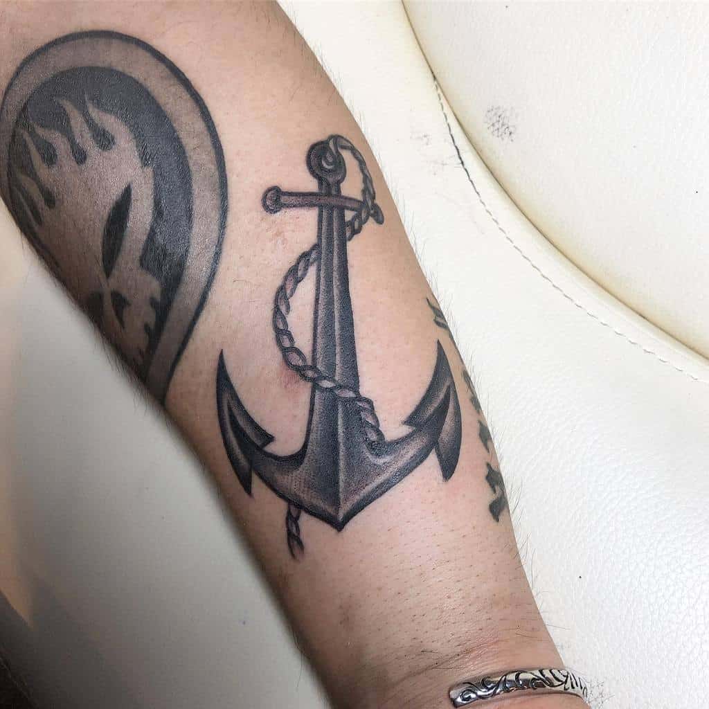 Tattoo of a shaded anchor with a rope wrapped around it, inked on a person's forearm, pays homage to the navy heritage