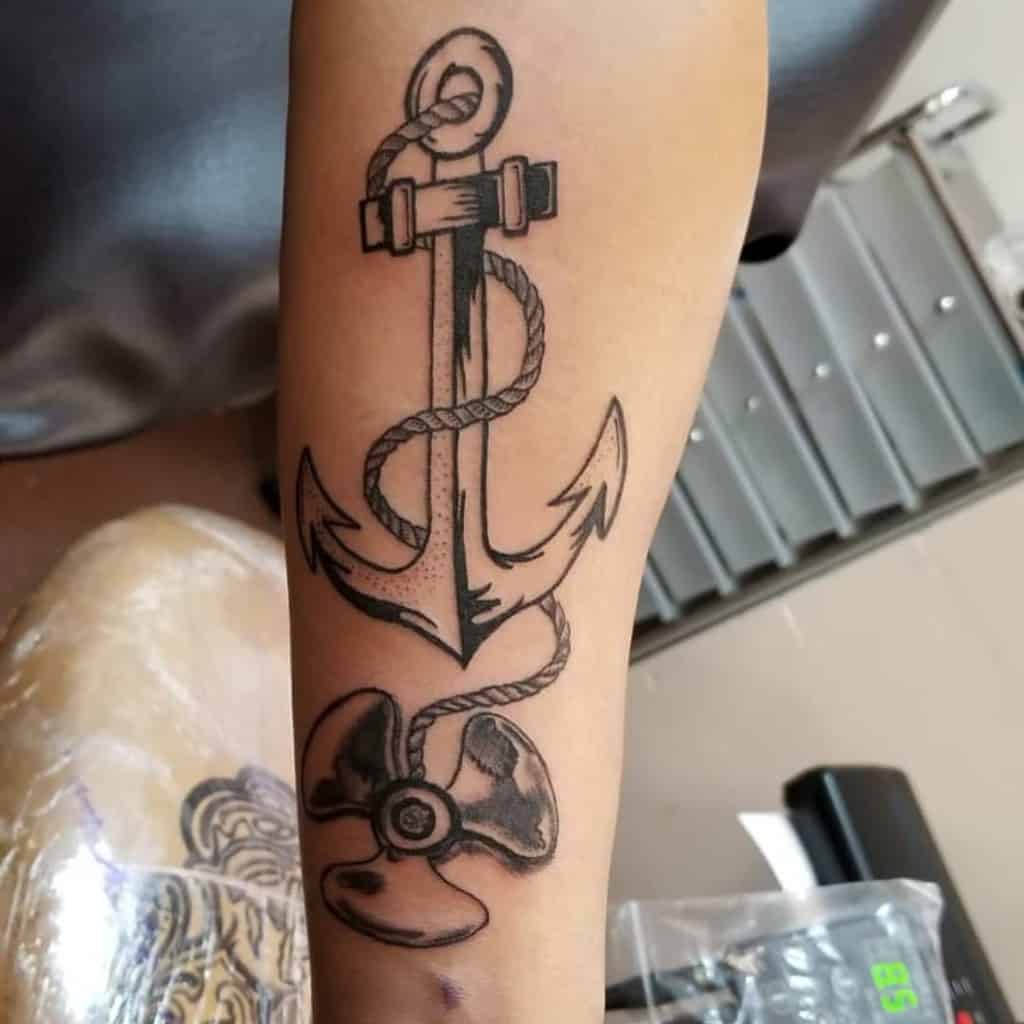 Black navy anchor tattoo with a rope and propeller on a person's forearm