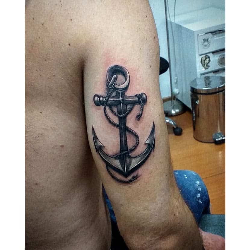 Tattoo of a detailed navy anchor with rope on a person's upper arm in a studio setting