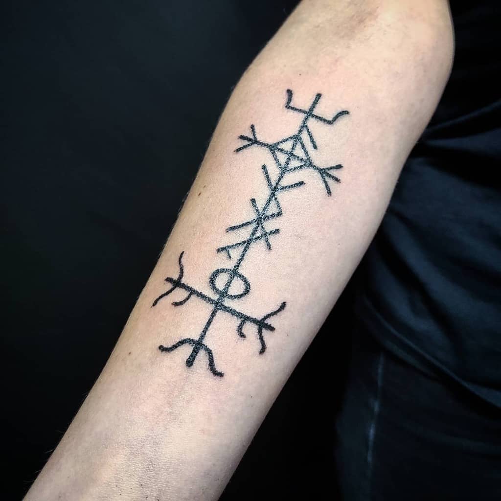 This forearm tattoo features a Nordic-inspired protection symbol, with intricate line work forming an elongated design