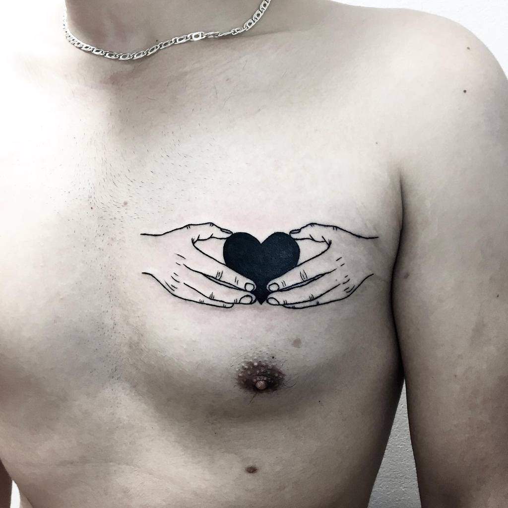 Tattoo depicting two hands cradling a solid black heart, symbolizing care and protection, rendered in fine line detail
