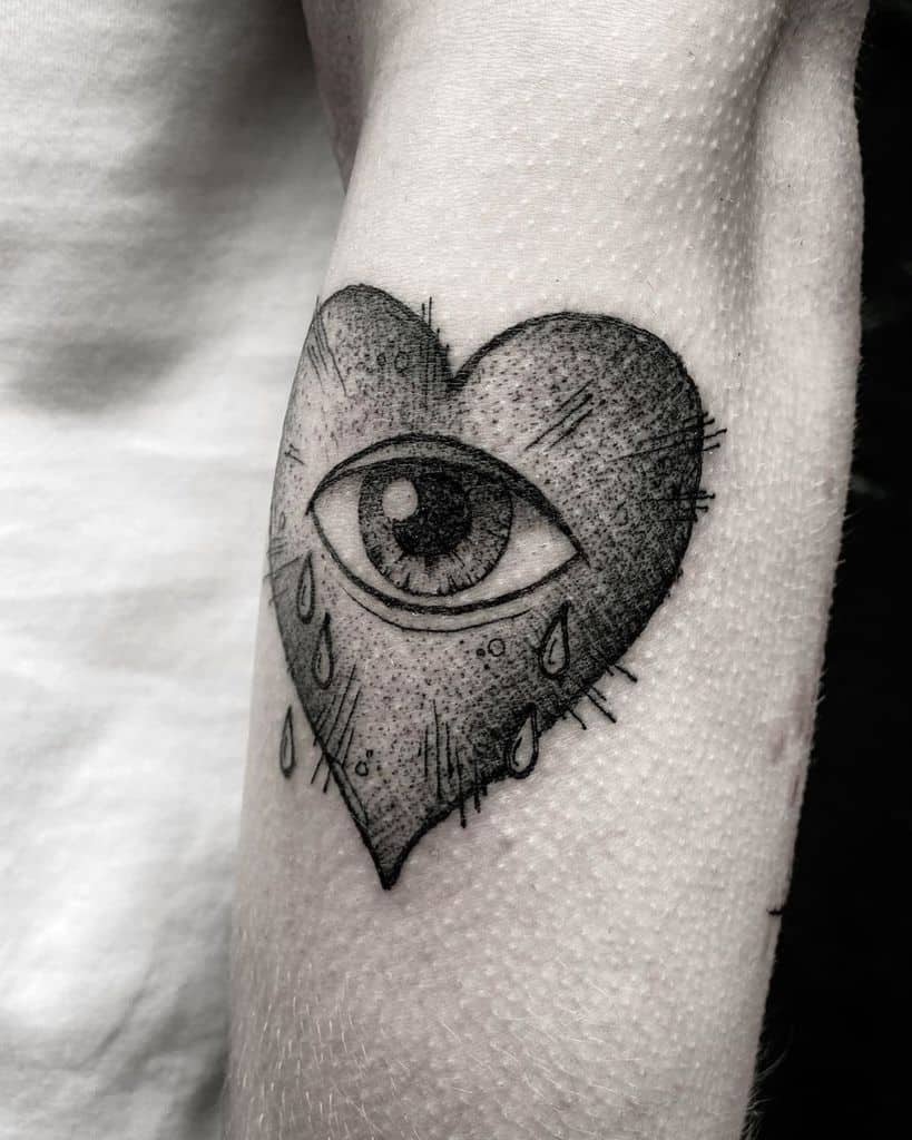 Black tattoo of a heart with an eye in the center, surrounded by teardrops