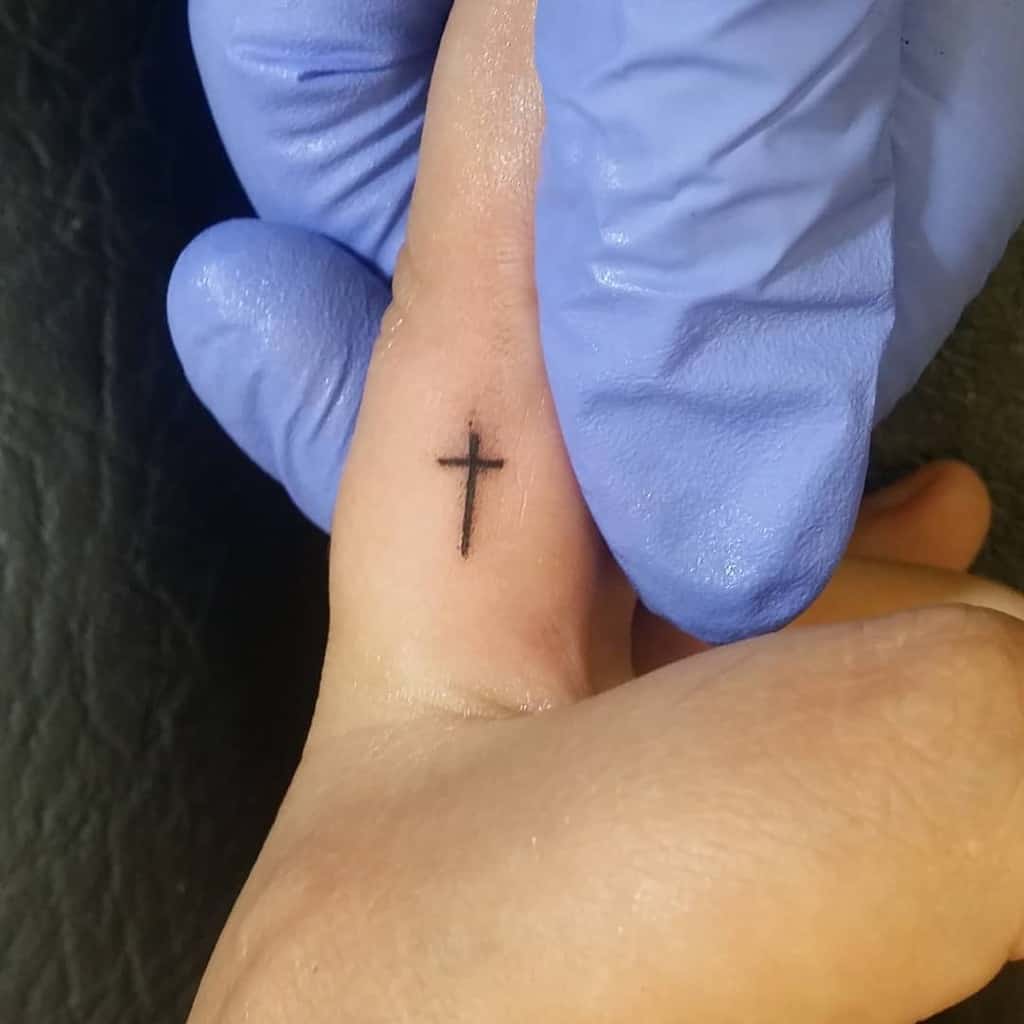 Small black cross tattoo on a finger